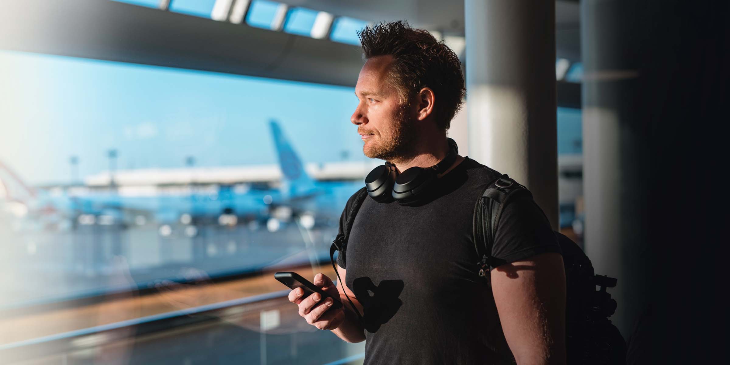 Mies seisoo lentokentällä matkapuhelin kädessään. 