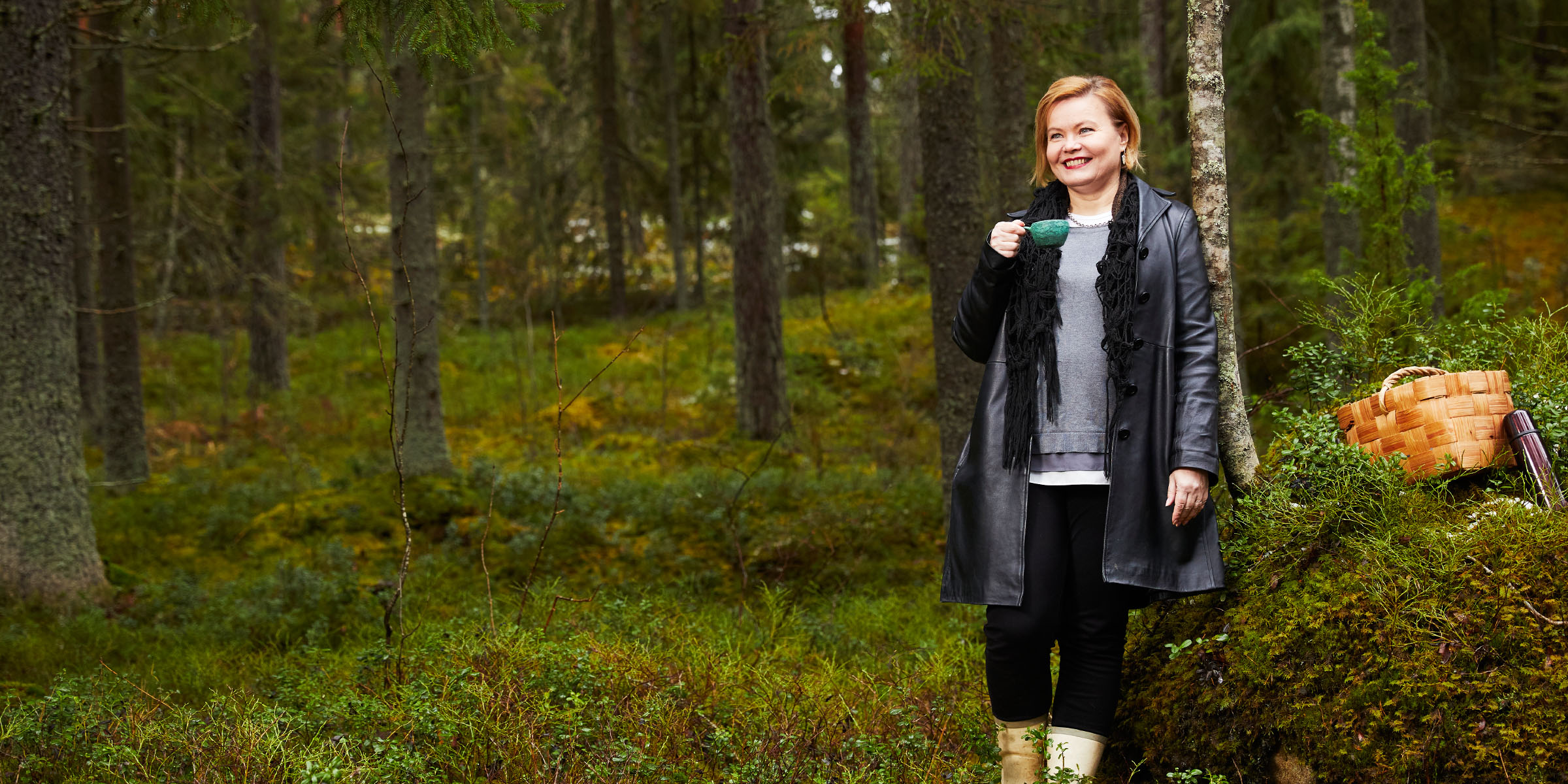 Aivotutkija Minna Huotilainen hymyilee metsässä kuksa kädessään. 