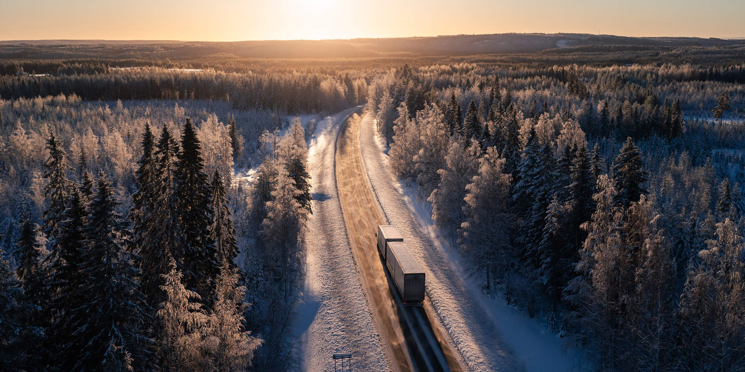 Rekka kulkee Suomen talvisella tiellä auringon noustessa.