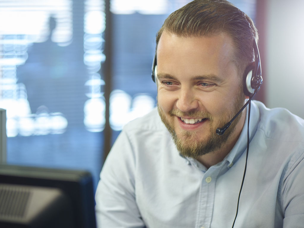 Hymyilevä mies kuulokkeet päässään ja puhuu mikrofoniin