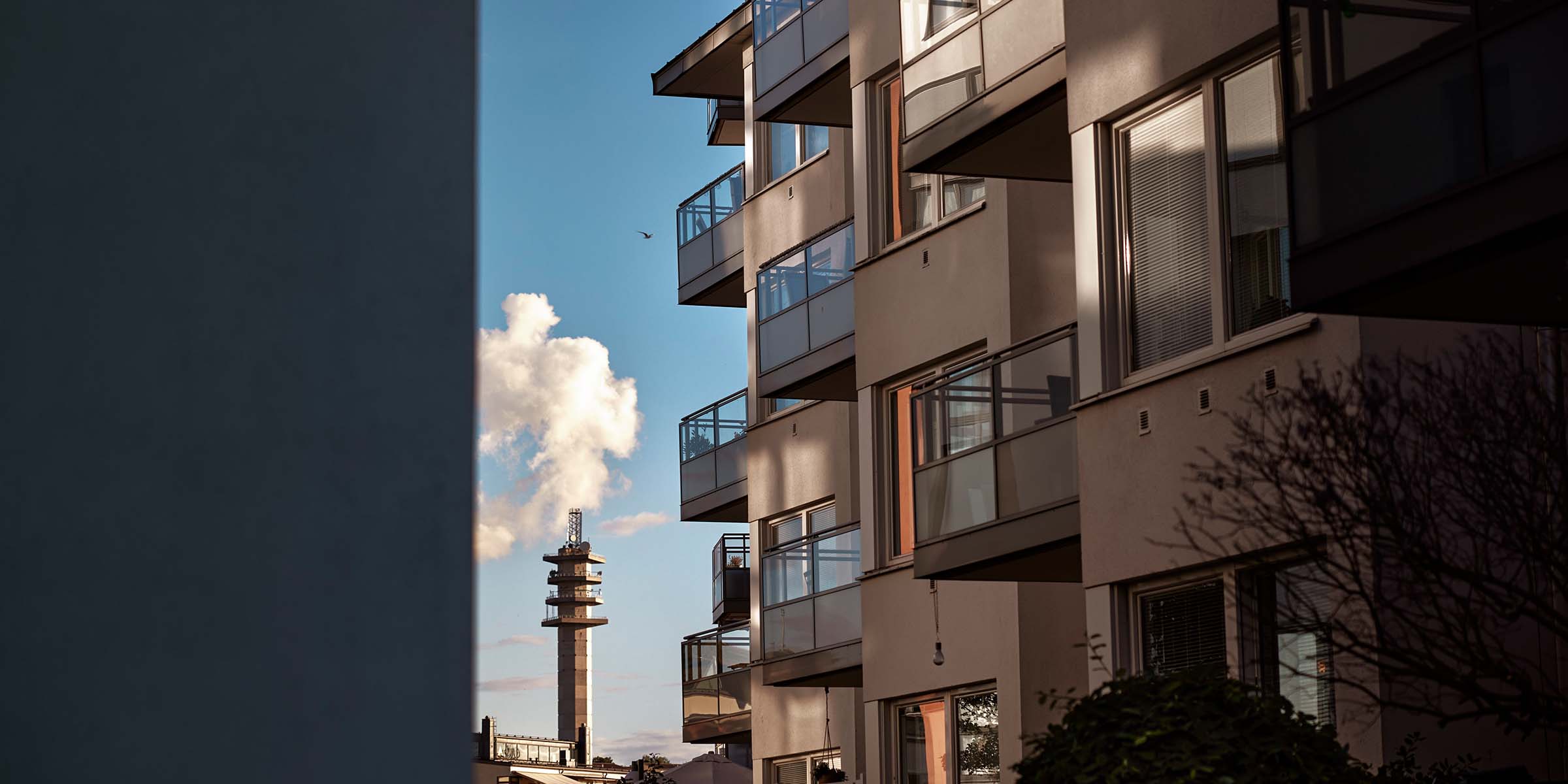 Kerrostalon etuseinää, parvekkeenlaseista heijastuu aurinko. 